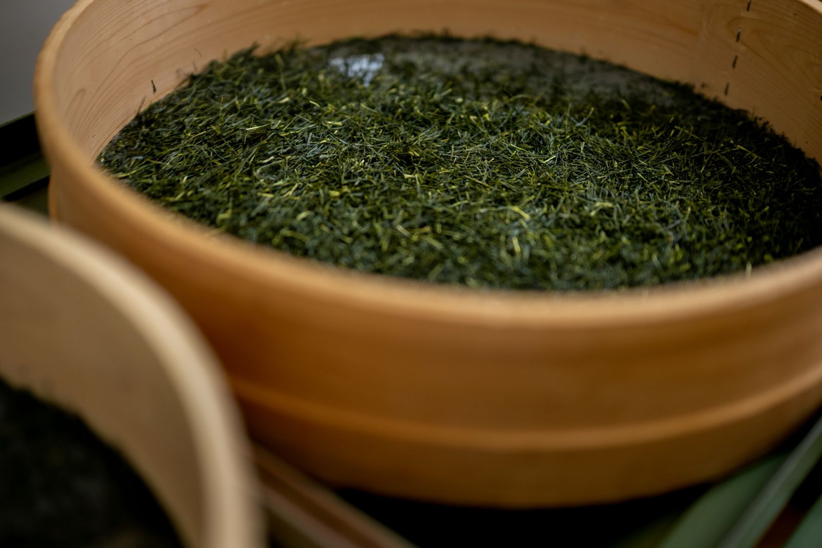 Finished sencha leaves resting in a traditional wooden tea bucket at the Sasaki Seicha facility.