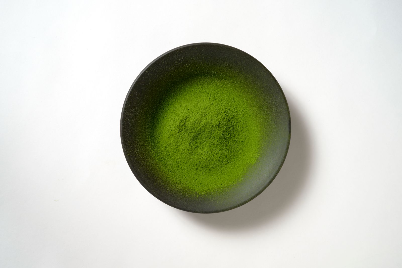 Vibrant green matcha powder in a dark ceramic bowl, stone-ground at the Sasaki factory in Kakegawa