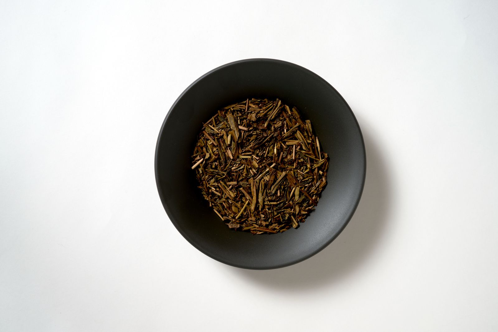 Roasted hojicha leaves and stems in a dark ceramic bowl, showcasing the warm reddish-brown color achieved through charcoal roasting