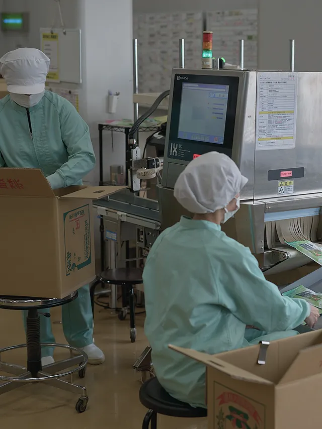 Workers packing finished tea past an X-ray inspection machine for shipment.